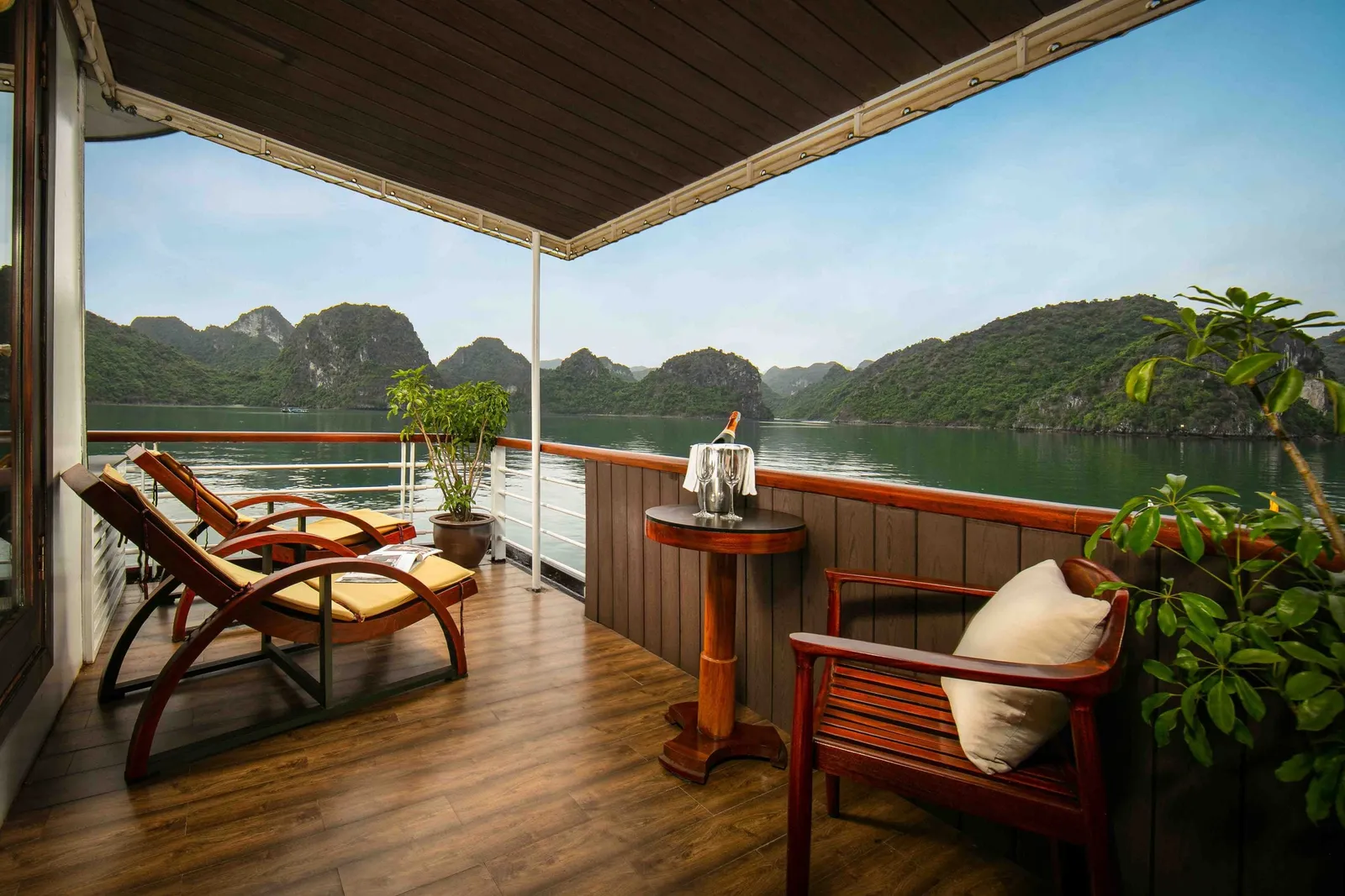 A wooden deck terrace with lounge chairs and seating overlooking calm water and distinctive limestone karst mountains.
