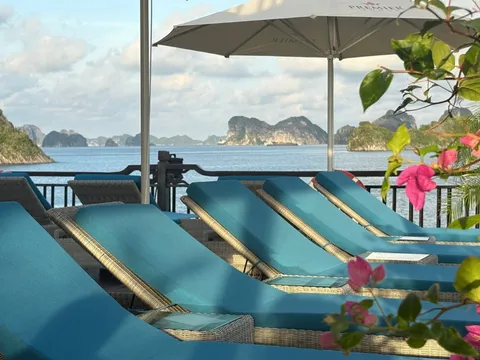 Teal sun loungers under a white umbrella, bougainvillea in the foreground and karst on the horizon