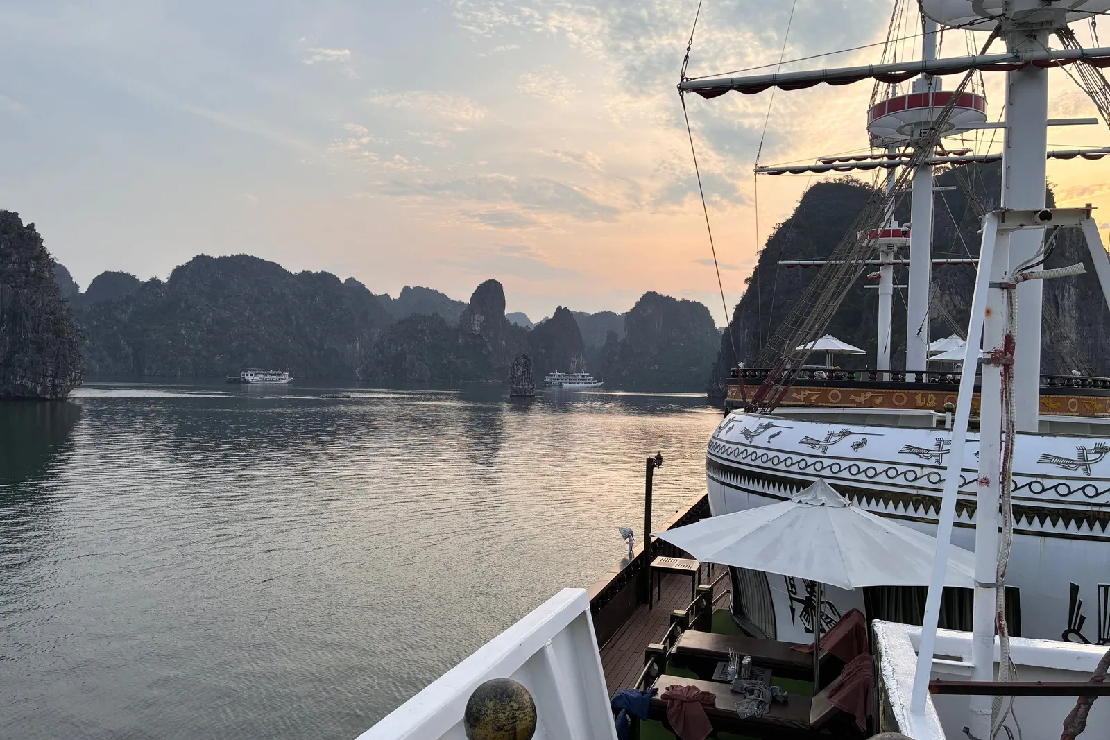 Looking forward along the deck at dusk, rigging and masts against a pale sky over the bay