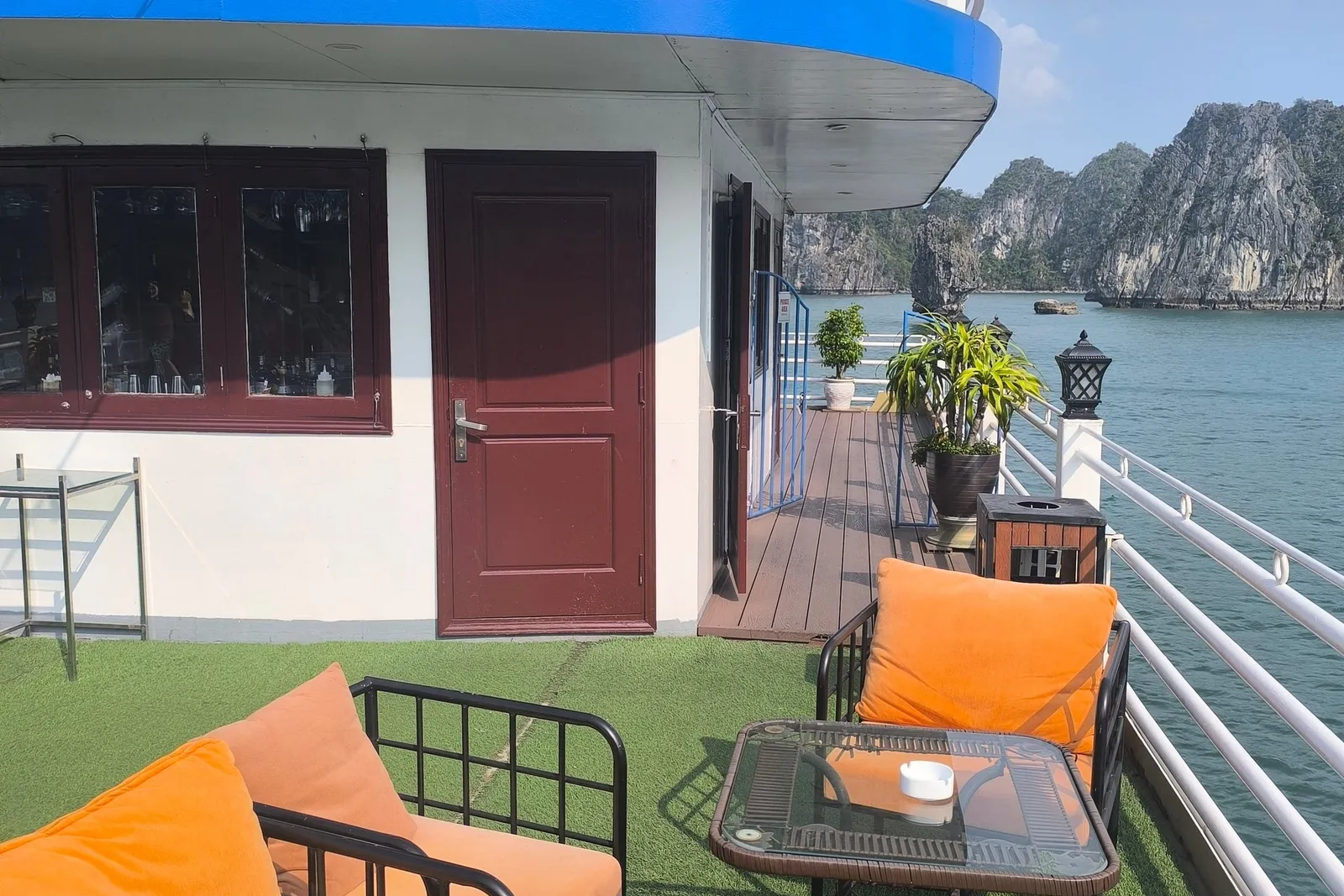 Sheltered deck corner with orange cushioned seats beside the cabin door, the bay to the right