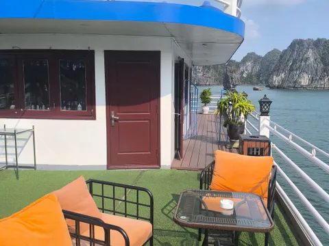 Sheltered deck corner with orange cushioned seats beside the cabin door, the bay to the right
