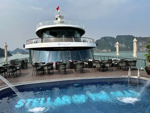Pool deck set with dining tables under white umbrellas, the ship name laid into the pool floor