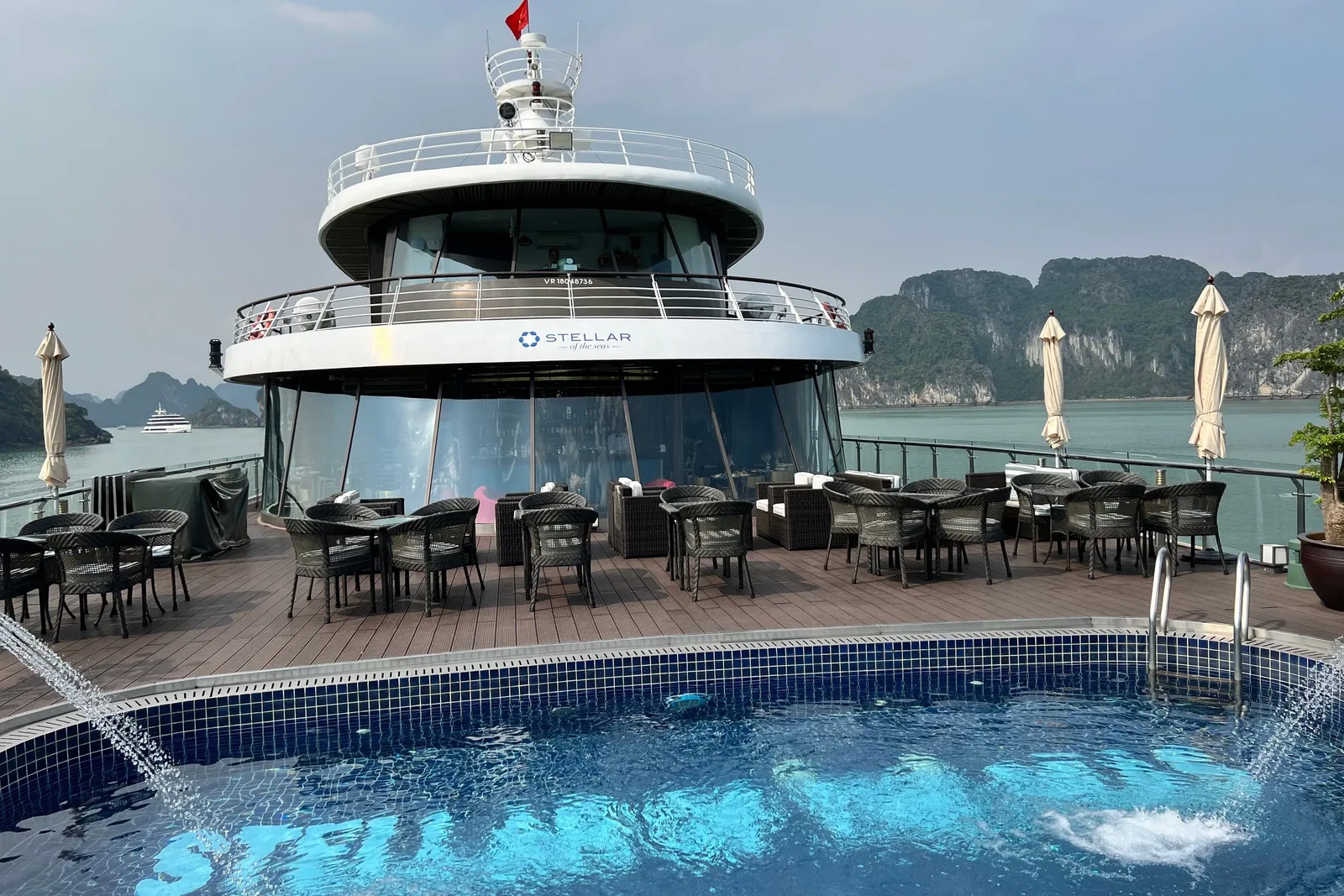 Pool deck set with dining tables under white umbrellas, the ship name laid into the pool floor