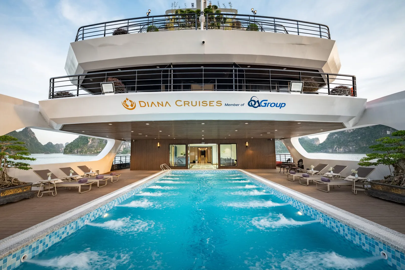 A swimming pool on the deck of a cruise ship with limestone karsts visible in the background and the name Diana Cruises painted on the ship's structure.