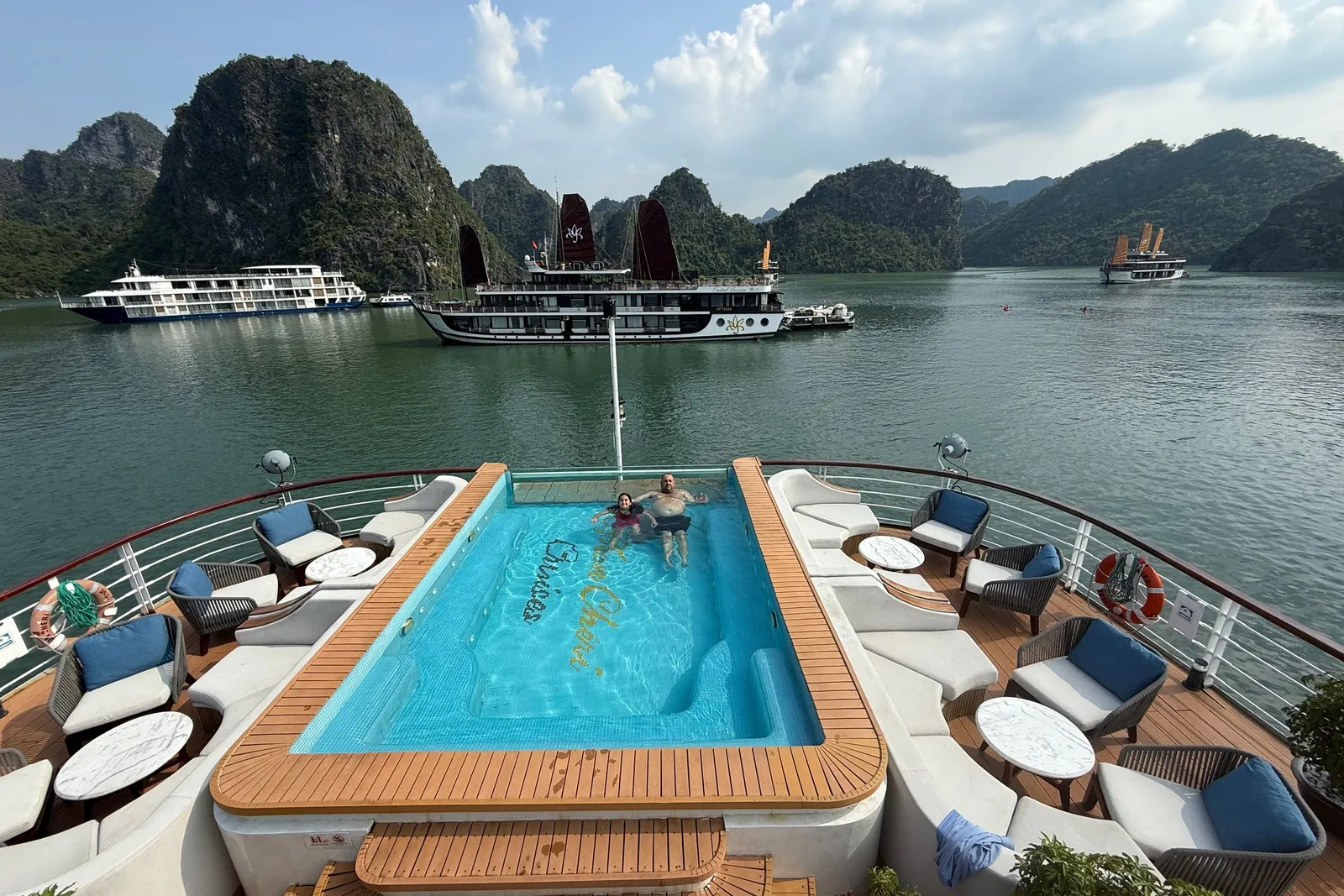 Sundeck pool ringed with cushioned seating, timber decking around it and junks at anchor beyond