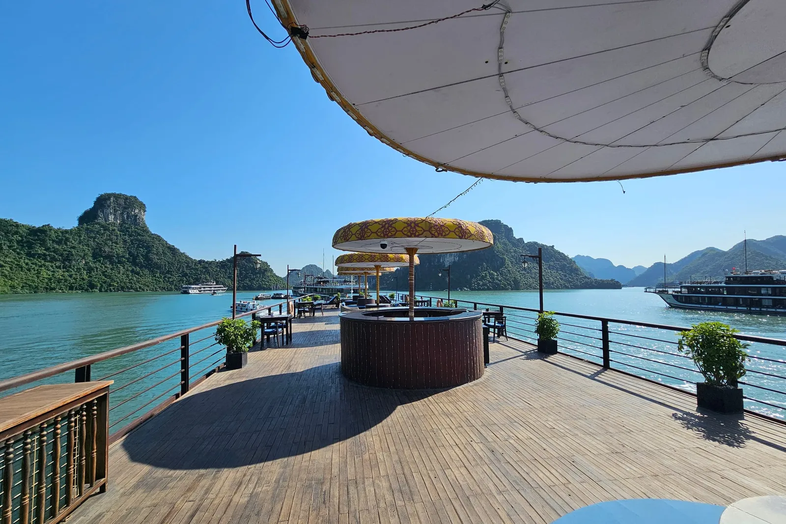 Foredeck shaded by a white awning, a gilded canopy seat at the rail and open water past it