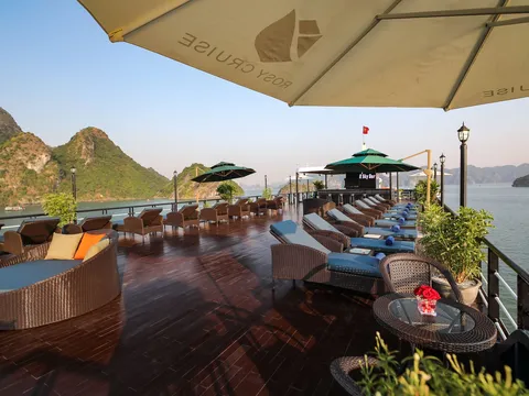 Sundeck lined with loungers under branded parasols, a low table with a red flower in front, the bay and karst beyond the rail