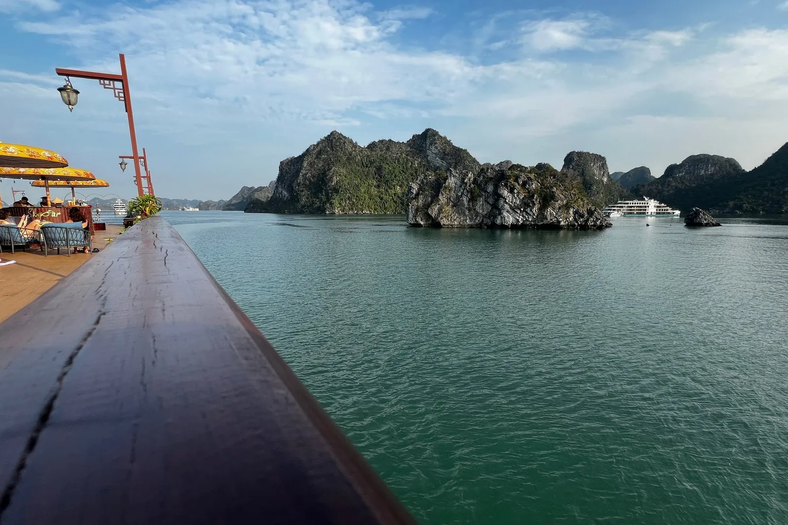 Along the deck rail at midday, karst islands standing out of flat pale water
