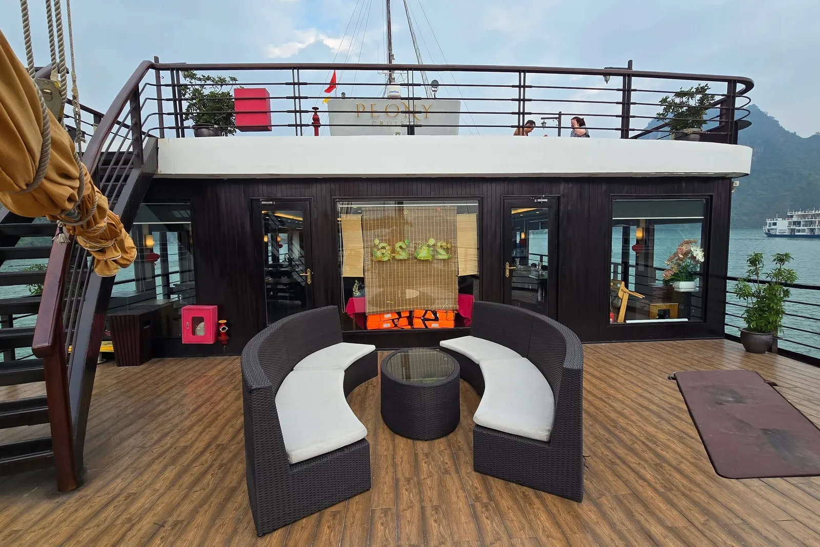 Upper deck lounge with curved rattan seats around a low table, the mast and bridge behind
