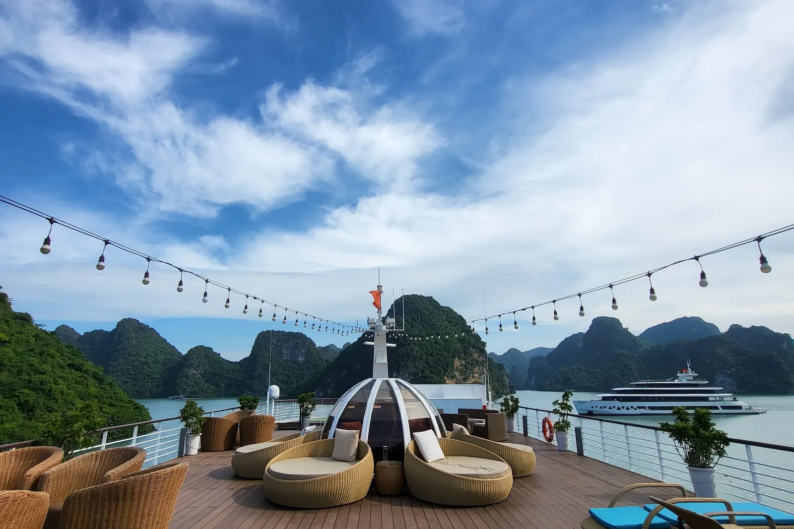 Timber deck with a domed daybed and string lights strung overhead, karst islands beyond the rail