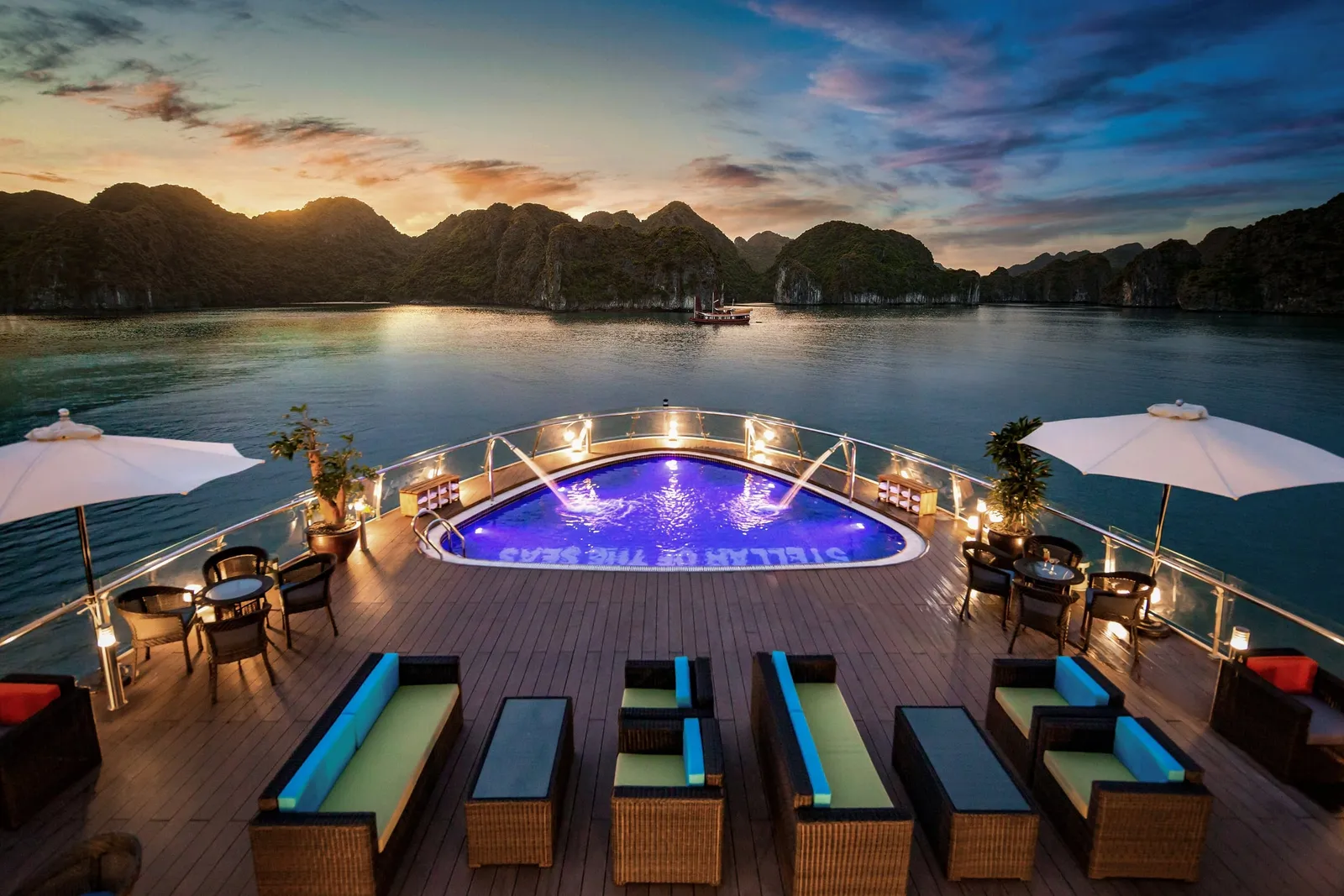 The pool lit from within at dusk, umbrellas up and the sun going down behind the karst