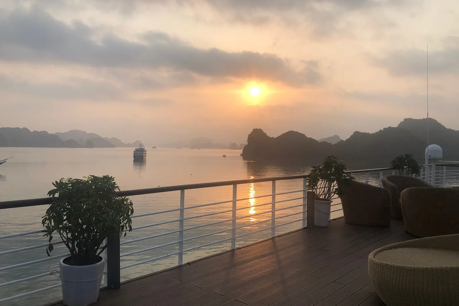 Sunrise from the upper deck, potted plants in the foreground and the sun coming up through haze over the bay