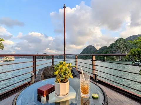 Drink on a deck table beside a potted plant, karst islands filling the view over the rail