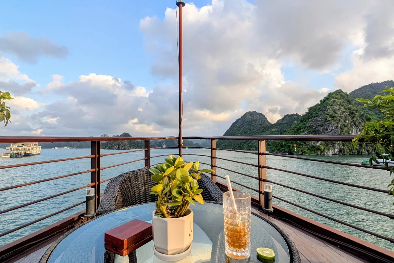 Drink on a deck table beside a potted plant, karst islands filling the view over the rail
