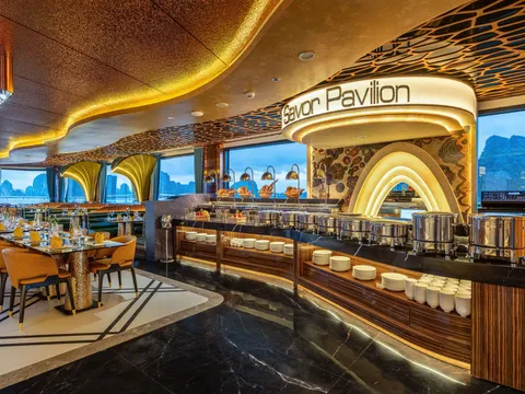 Buffet pavilion with a gold arch over the counter, mustard chairs at set tables and the bay through the windows