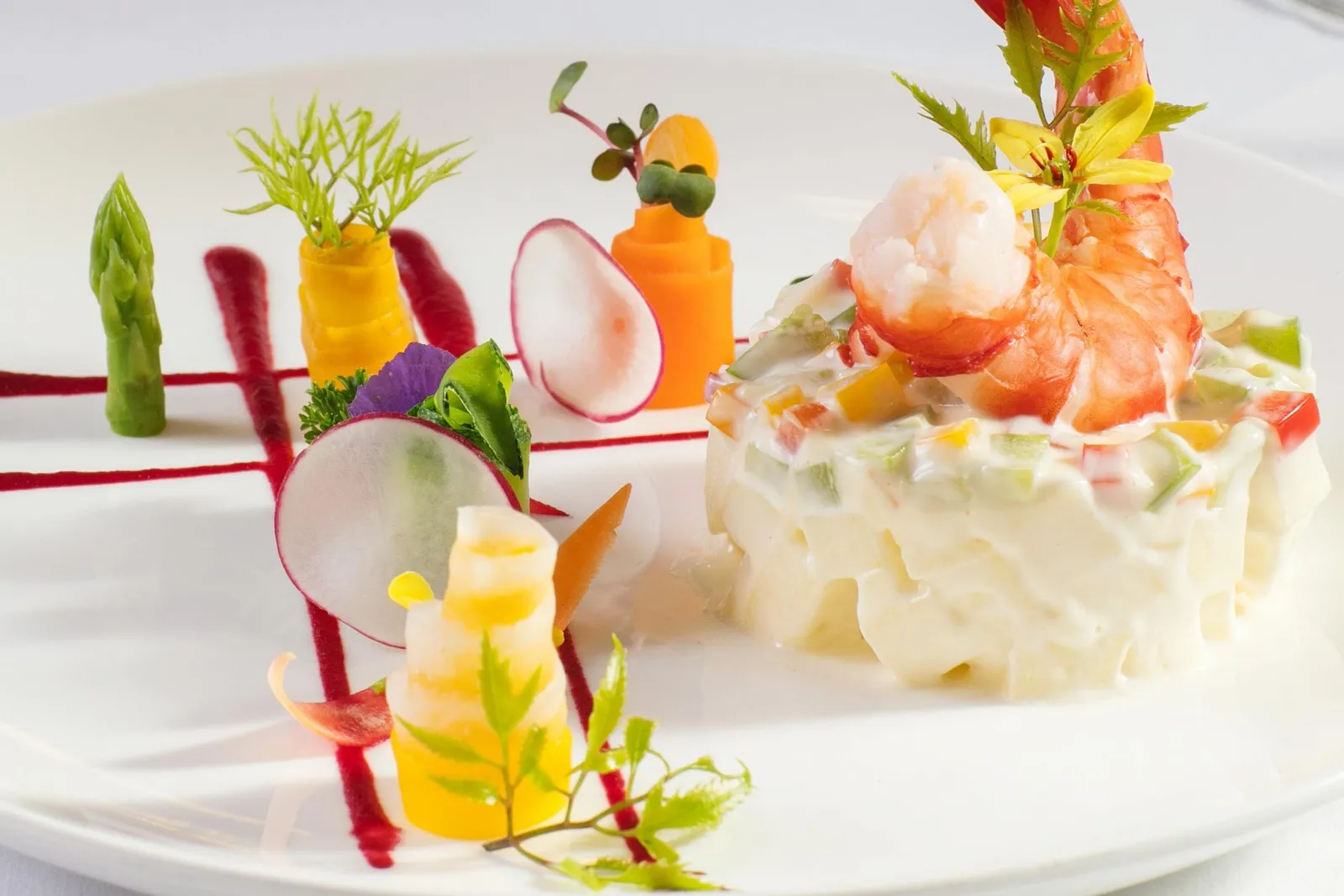 An elaborately plated gourmet dish with carved vegetables, shrimp, and decorative garnishes on a white plate.