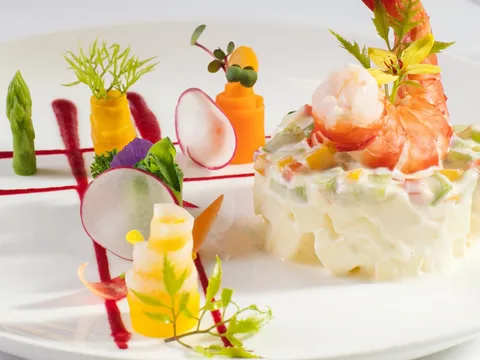 An elaborately plated gourmet dish with carved vegetables, shrimp, and decorative garnishes on a white plate.
