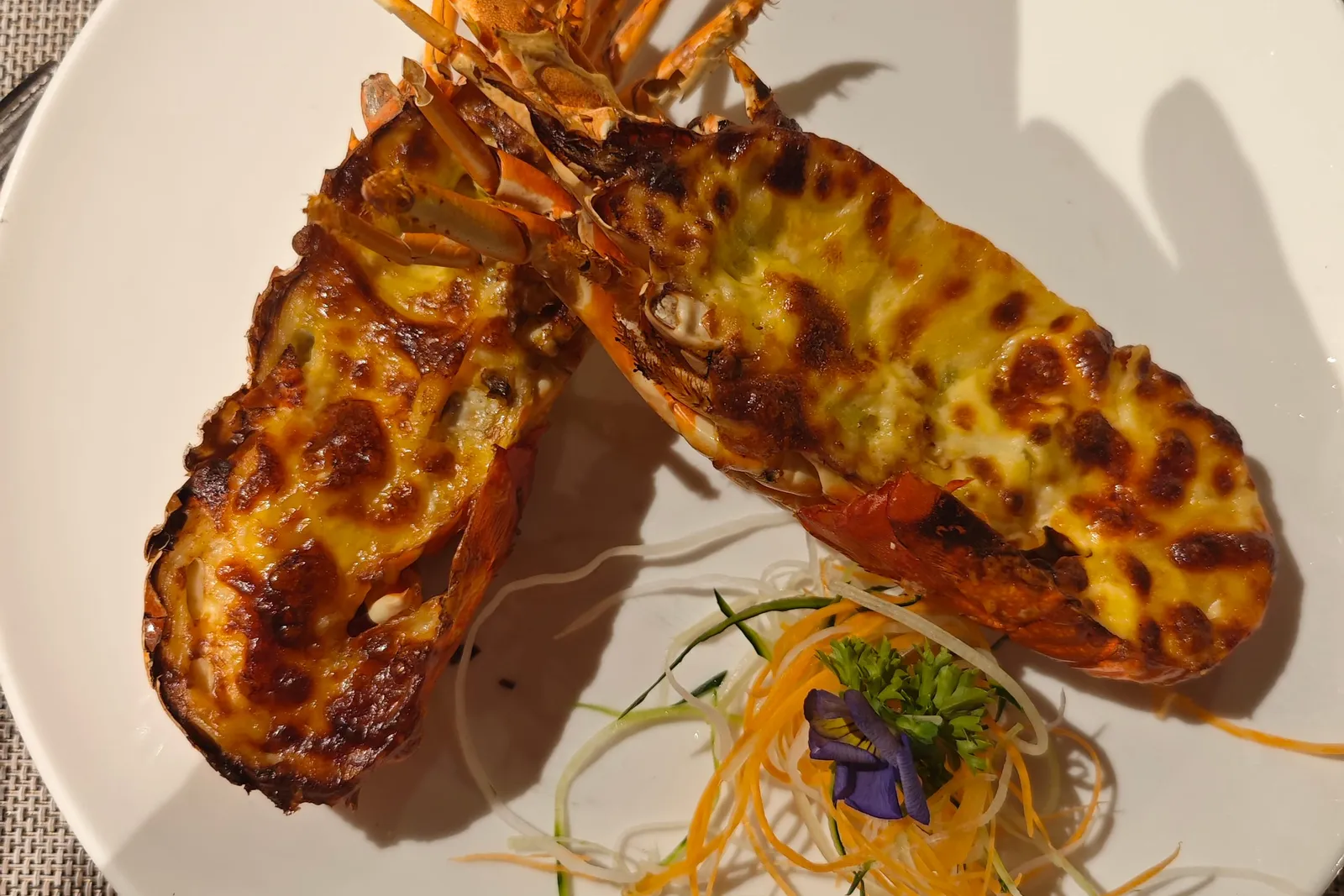 Grilled lobster split in half and plated with a garnish of shaved carrot