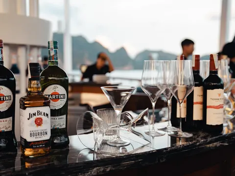 A bar setup with liquor bottles, wine bottles, and glassware on a dark counter with karst limestone peaks visible through windows in the background.