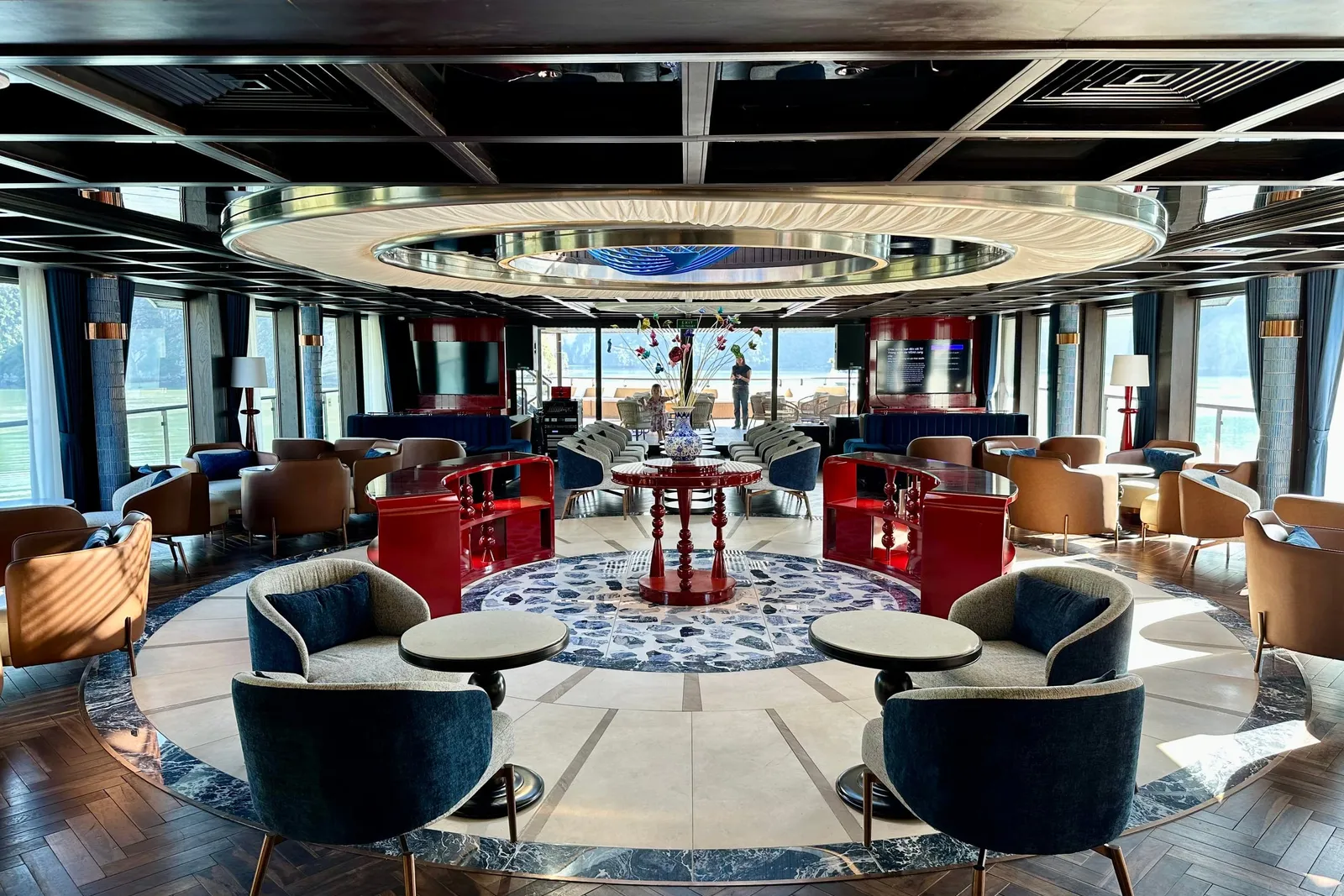 Lounge under a ring-lit ceiling, low chairs in red and navy grouped around tables