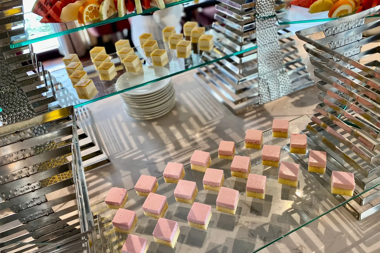 Dessert counter with rows of layered pink and yellow squares on a mirrored glass stand