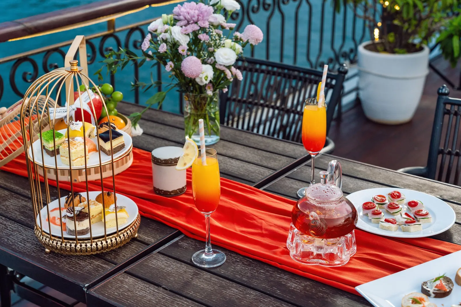 Afternoon tea on the deck: a tiered stand, a glass teapot and juice, flowers on the table