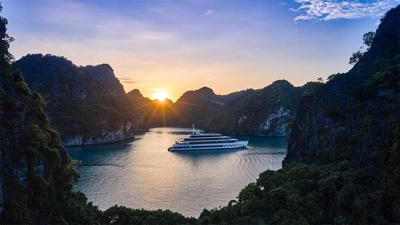 Elite of the Seas at anchor in a narrow channel, the sun coming up between two forested karst islands