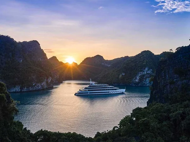 Elite of the Seas at anchor in a narrow channel, the sun coming up between two forested karst islands
