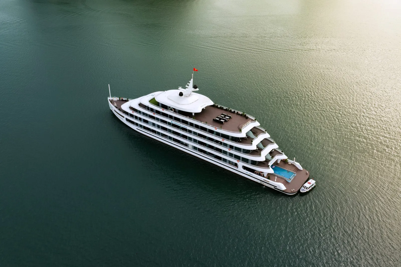 Catherine seen straight down from the air, five white decks and a pool on the stern, alone on olive-green water