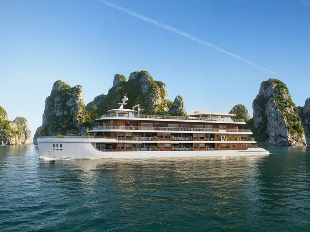 A large white and wood-paneled cruise ship sails through calm green water surrounded by tall limestone karst formations under a clear blue sky.