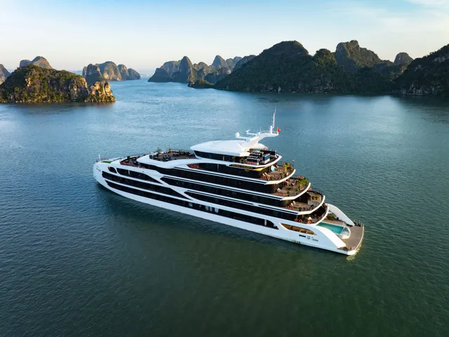 Aerial view of a white multi-deck cruise ship with a pool on the lower deck, sailing among limestone karst islands in calm green-blue water.