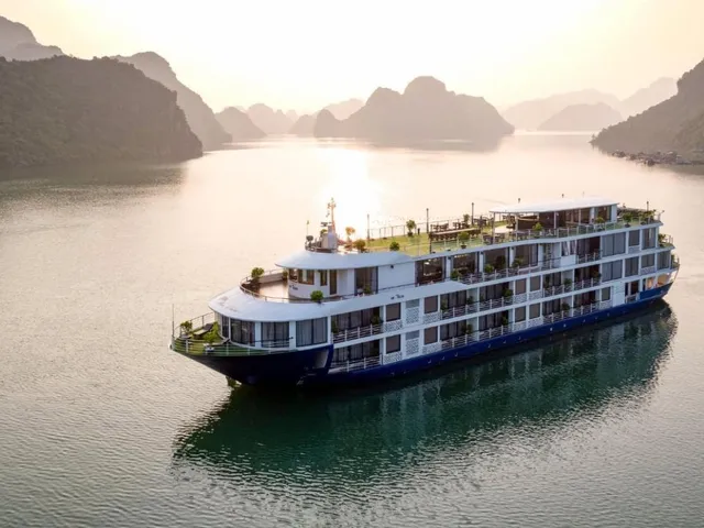 Mon Chéri at anchor in gold evening light, four white decks and the sun low behind the karst