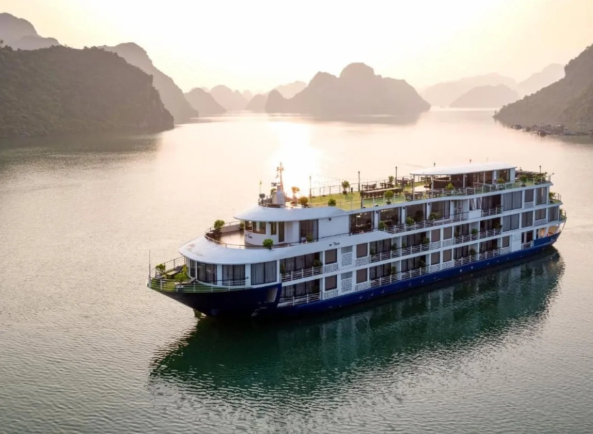 Mon Chéri at anchor in gold evening light, four white decks and the sun low behind the karst