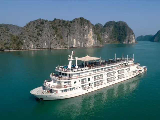 A white multi-deck cruise ship floats in turquoise water surrounded by limestone karst islands.