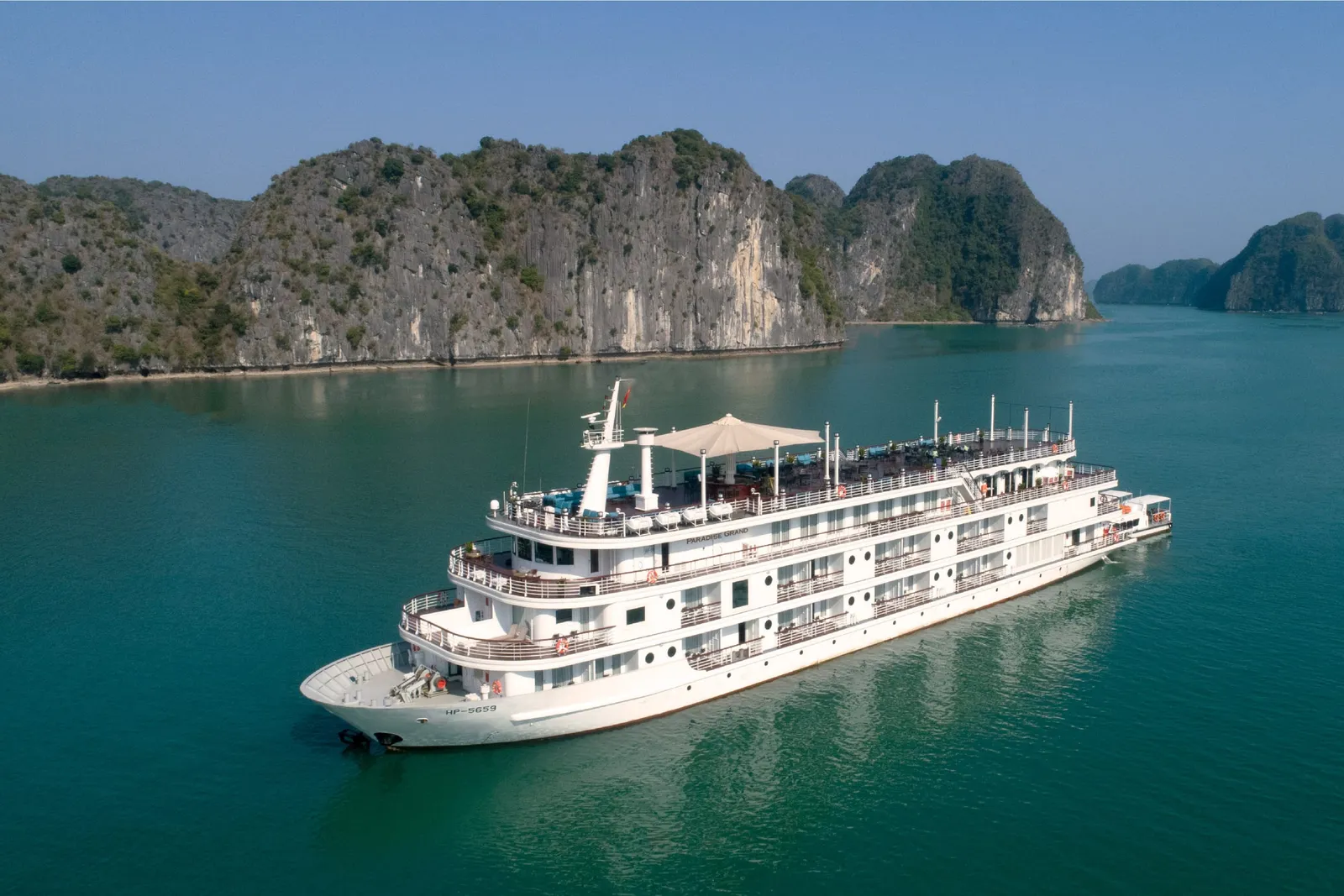A white multi-deck cruise ship floats in turquoise water surrounded by limestone karst islands.