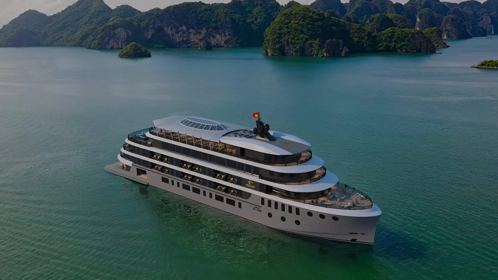 An aerial view of a large multi-deck white cruise ship with a Vietnamese flag on calm green water, with forested limestone karst islands in the background and a small logo emblem on the vessel's side.