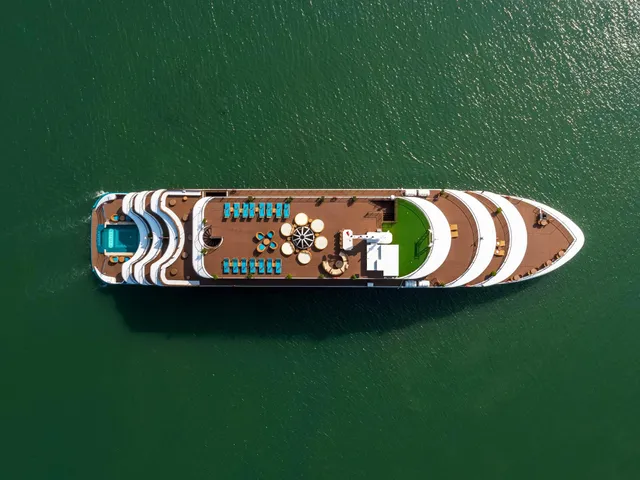 Capella seen straight down from the air, the whole white hull and its stern pool laid out on flat green water