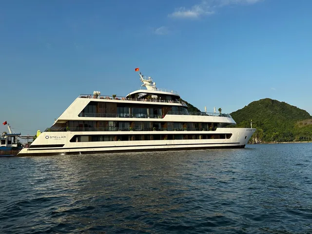 Stellar of the Seas broadside on calm water, the ship name on the white hull and karst islands behind