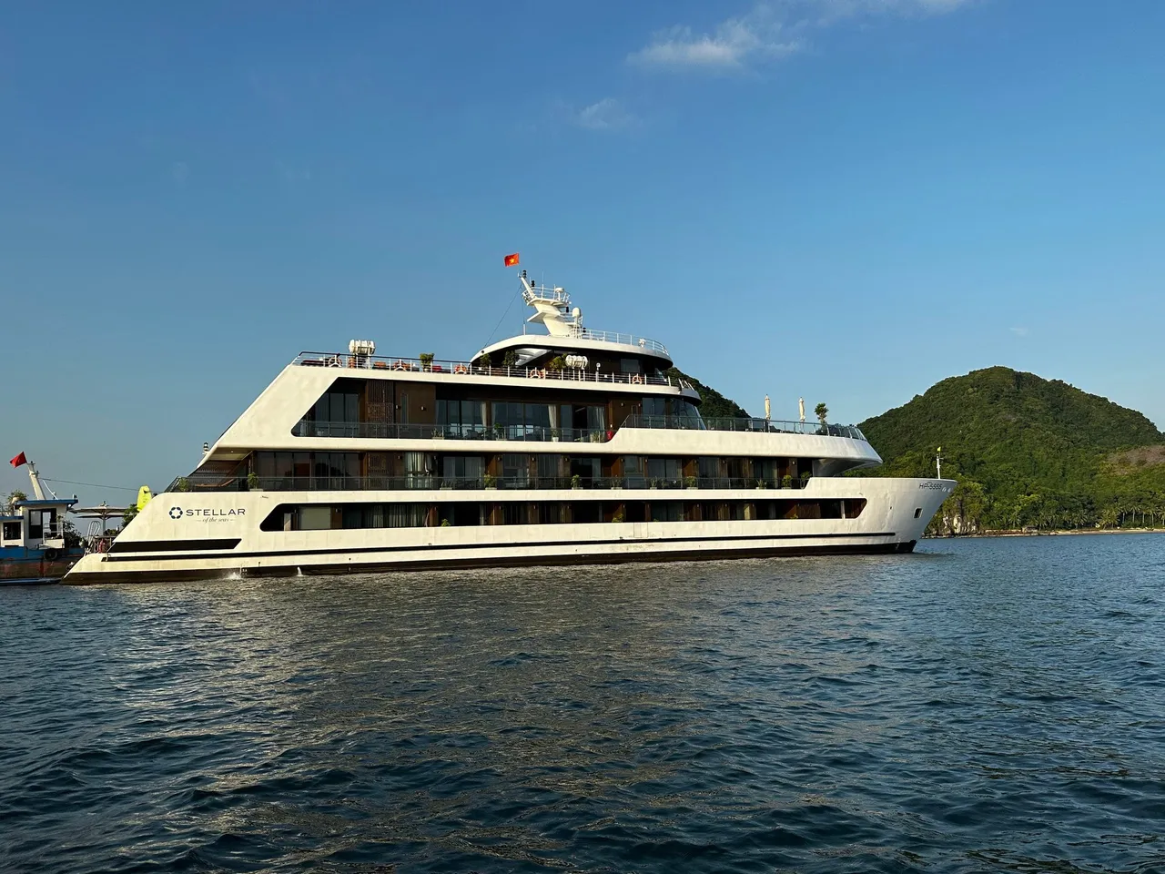 Stellar of the Seas broadside on calm water, the ship name on the white hull and karst islands behind