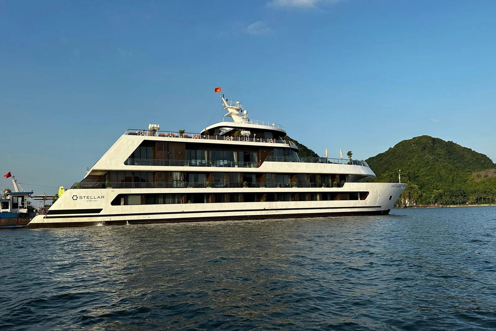 Stellar of the Seas broadside on calm water, the ship name on the white hull and karst islands behind