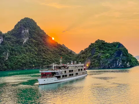 Capella under way at sunset, the sun dropping behind a karst island and the water turned copper