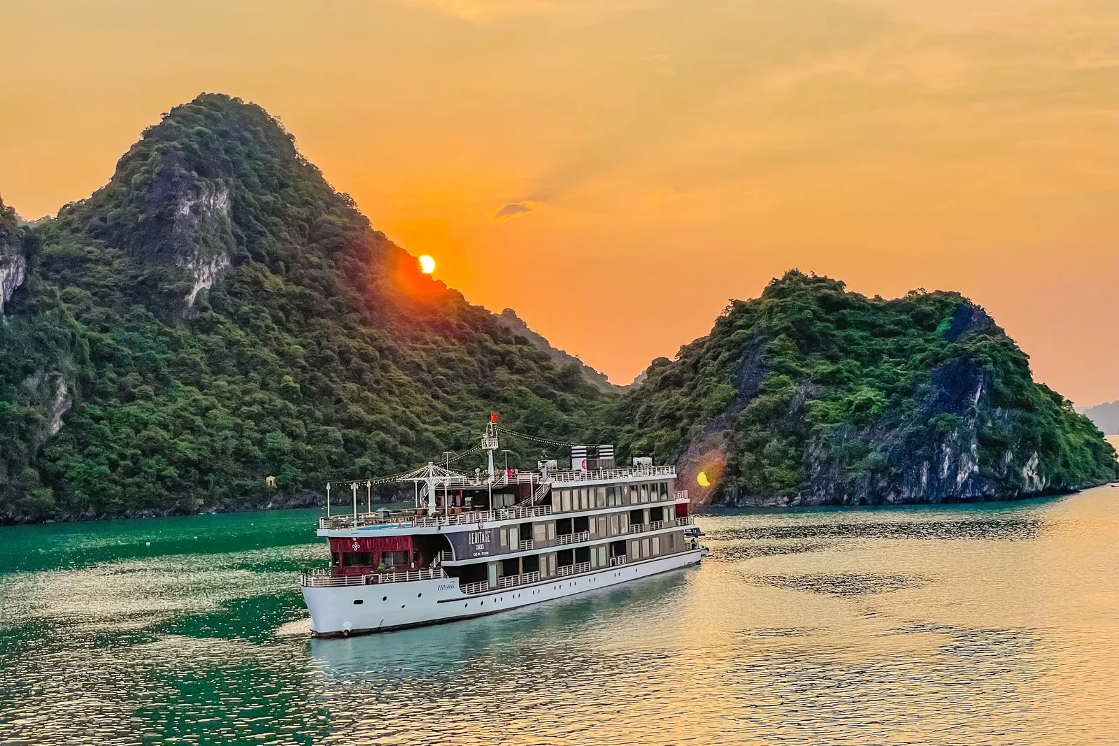 Capella under way at sunset, the sun dropping behind a karst island and the water turned copper