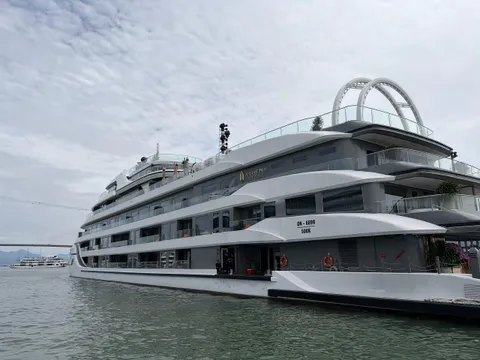 A large multi-deck white and grey cruise ship with the name 'Athena' on its hull and registration 'QN-6899' moored on grey-green water, with a bridge and another vessel in the distance under an overcast sky.