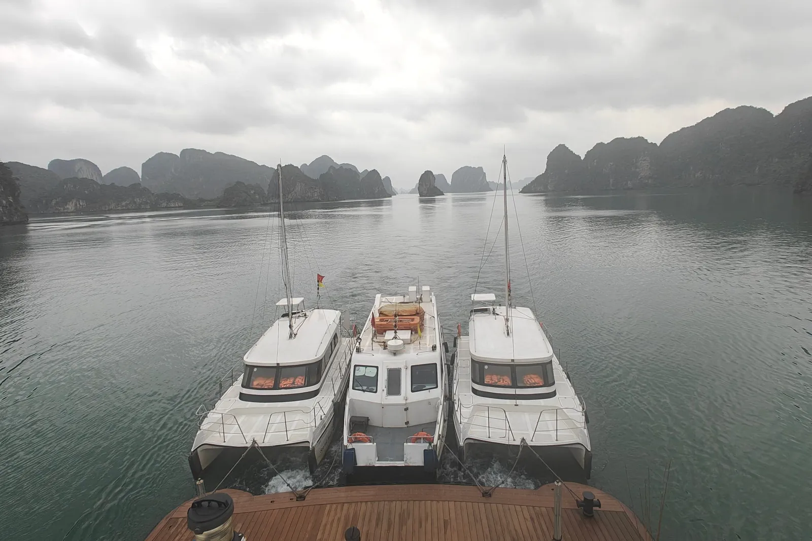 Three tenders moored side by side at the stern, seen from the deck above on a grey morning