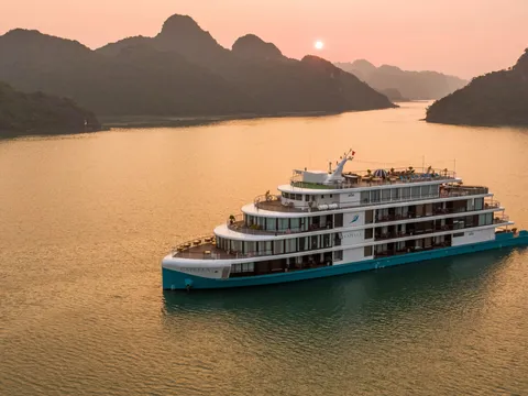 Capella alone on gold water at dusk, karst islands ranged along the horizon behind her