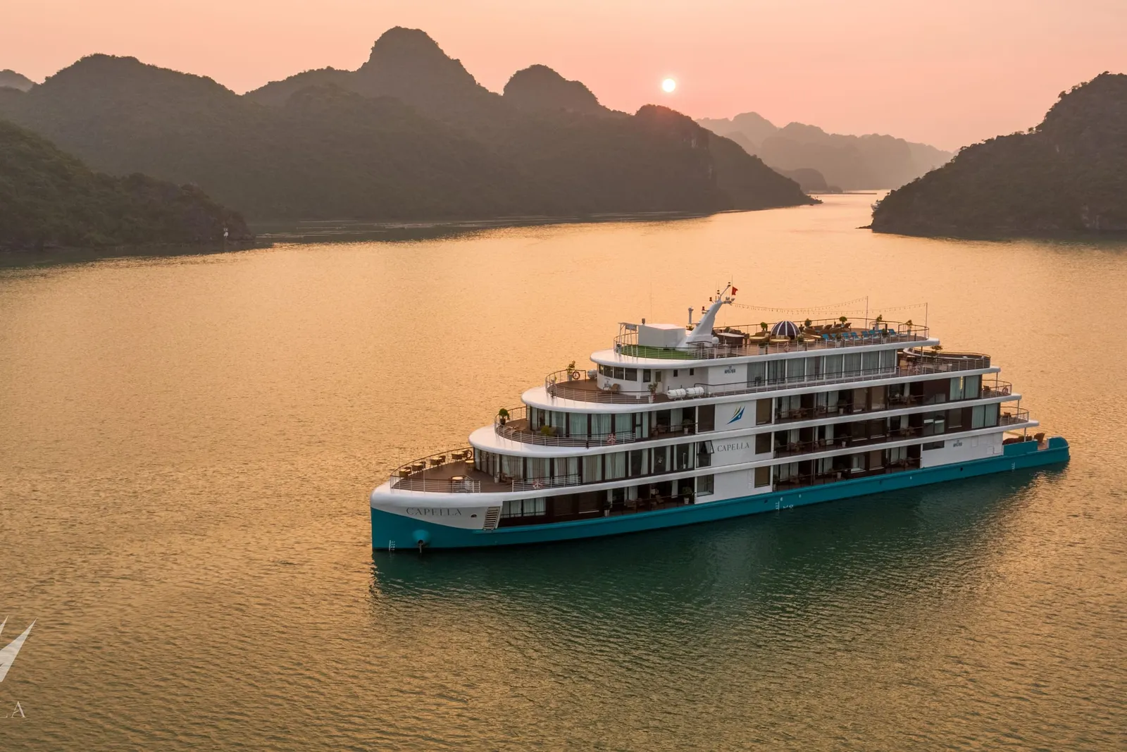 Capella alone on gold water at dusk, karst islands ranged along the horizon behind her