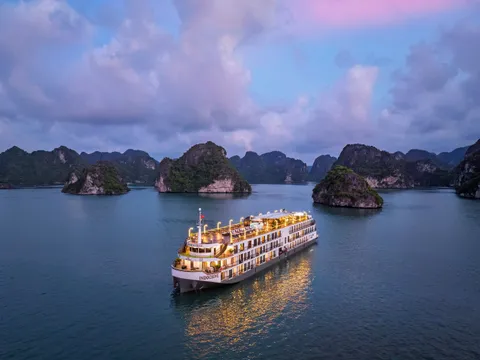 Indochine alone on still water under a violet sky, karst islands ranged along the horizon