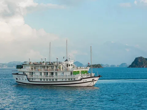 A multi-deck white cruise vessel with the name painted on its bow and a registration number on its stern, sailing on turquoise water with karst limestone islands in the background.