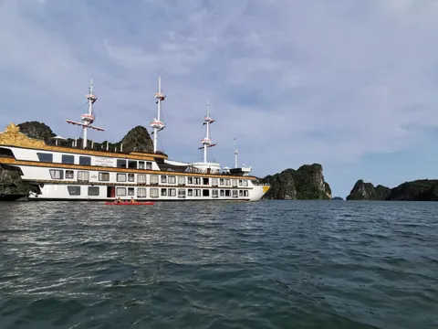Dragon Legend broadside under way, three masts over a dark hull and karst islands close behind