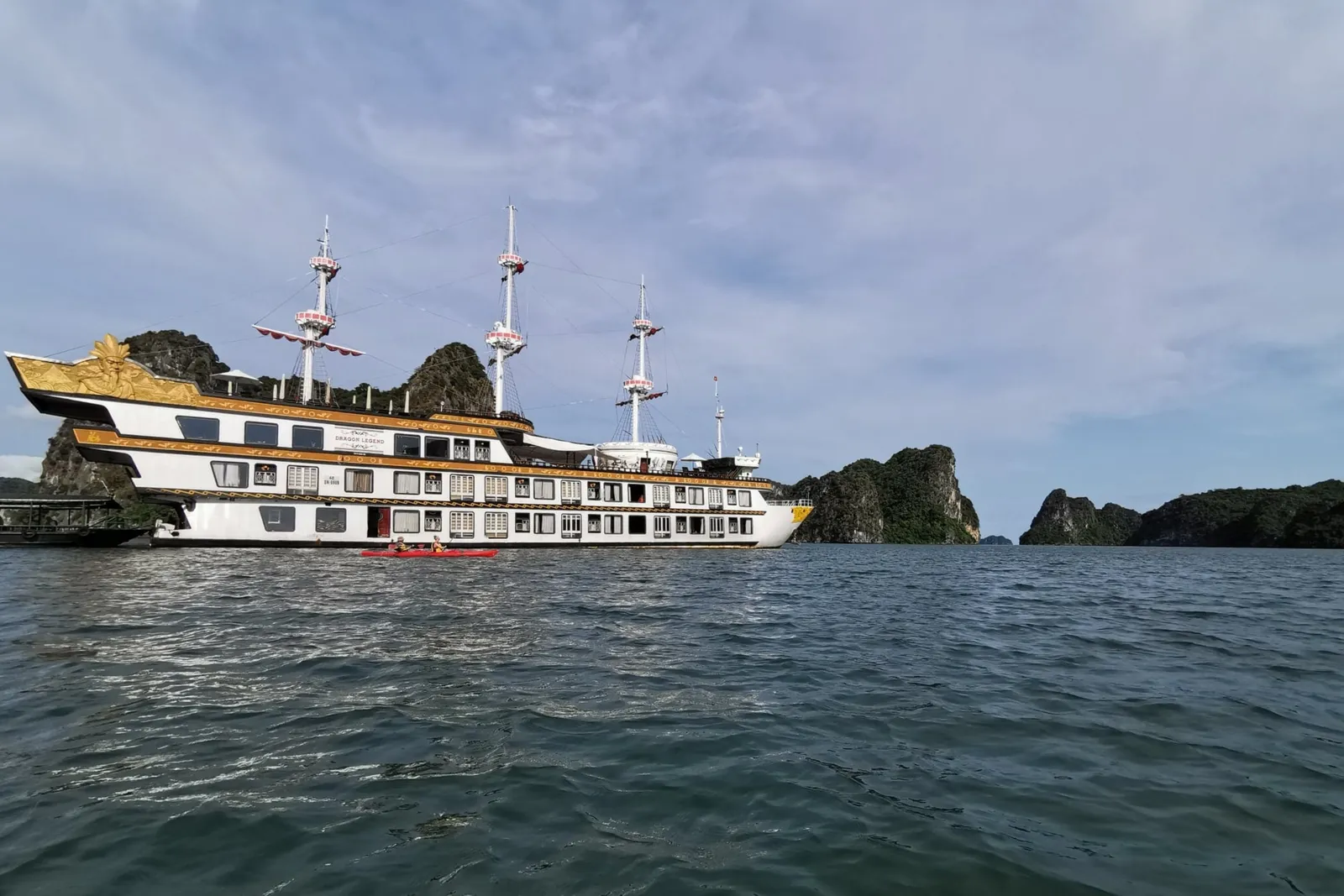 Dragon Legend broadside under way, three masts over a dark hull and karst islands close behind